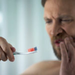 A man feeling the pain of gum disease. Learn more about gum disease. What is it? How to precent it.