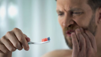 A man feeling the pain of gum disease. Learn more about gum disease. What is it? How to precent it.